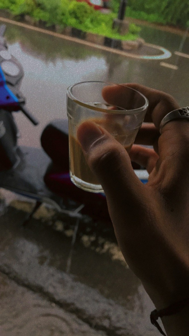 Eine Person hält ein Bierglas vor ein Fenster, daneben steht ein Motorroller und im Hintergrund sind Bäume, Pfosten und eine Straße zu sehen.