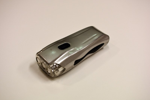 Ein silbern glänzender Elektroschocker mit metallischer Oberfläche, zentral auf einem weißen Tisch platziert.