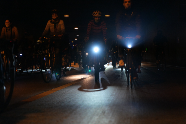 Eine Gruppe von Menschen, die nachts mit Fahrrädern durch eine Stadtstraße fahren und Helme tragen.