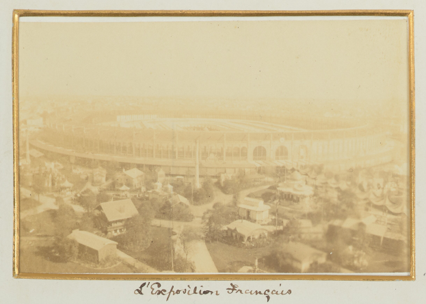 Altes Schwarz-Weiß-Foto eines Stadions, umgeben von Gebäuden, Bäumen und Strommästen mit Text unten.