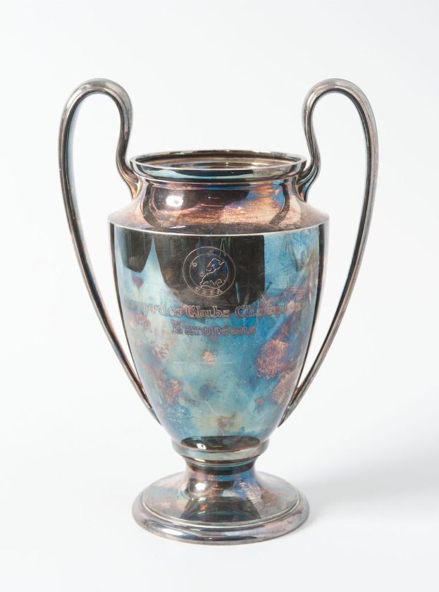 Der UEFA-Champions-League-Pokal, ein stählerner Pokal mit zwei Griffen und einem blauen und silbernen Farbschema, mit der Inschrift "UEFA Champions League", vor einem weißen Hintergrund.