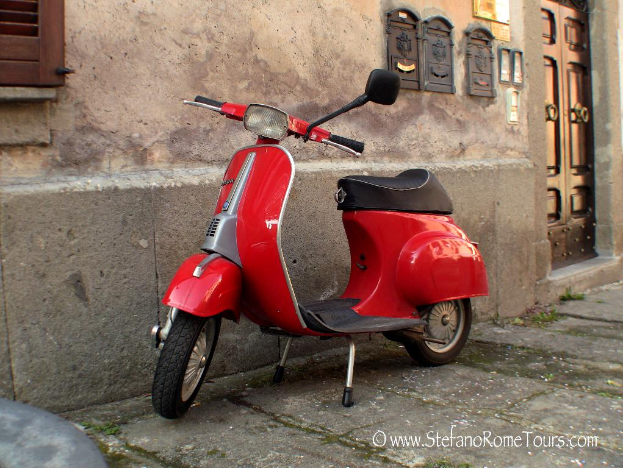 Ein rotes Rollerfahrrad steht vor einem Haus mit Tür und Fenstern auf einer Straße mit Text am unteren Bildrand.