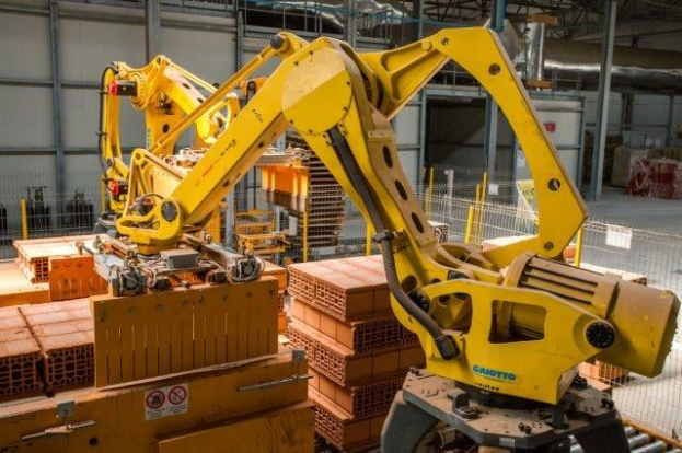 Großes industrielles Lagerhaus mit gestapelten Kisten, Überhead-Kränen, Zaun, Strommasten und einer fernen Wand in einer automatisierten Produktionsumgebung.