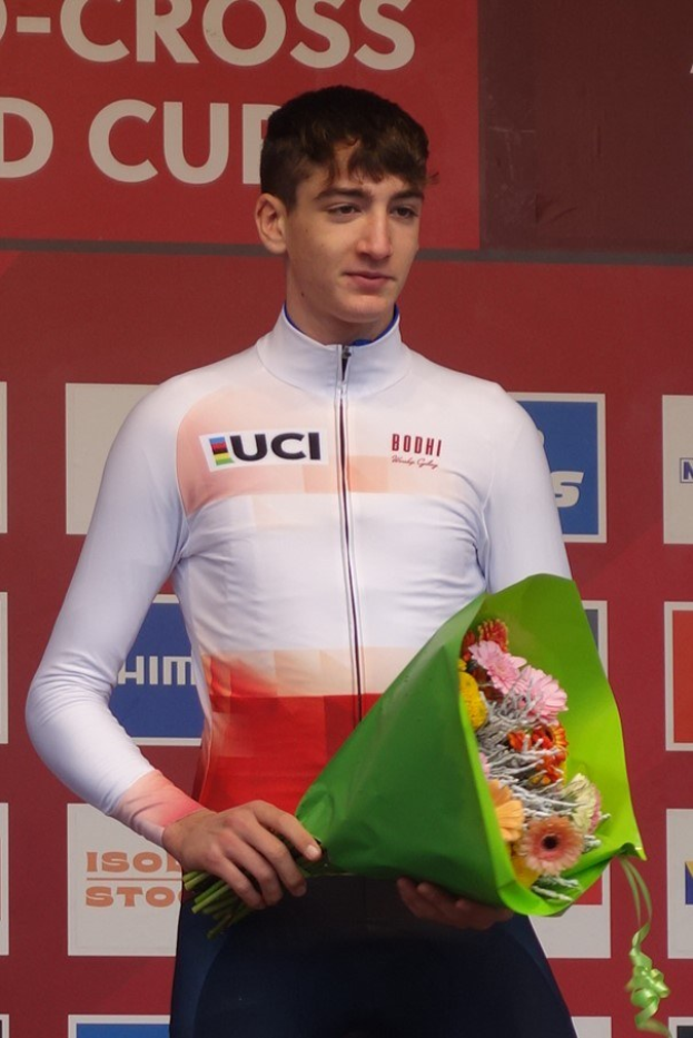 Ein Mann steht auf einem Podium und hält einen Blumenstrauß in den Händen, feiernd mit einem selbstbewussten und stolzen Gesichtsausdruck.