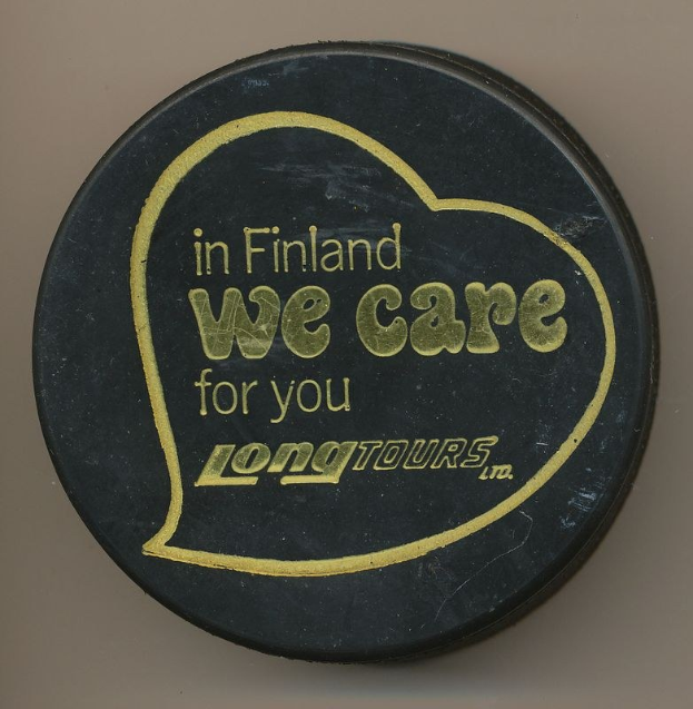 Schwarzer Hockey-Puck mit der Aufschrift "In Finland We Care For You Long Tours" vor einem cremefarbenen Hintergrund.