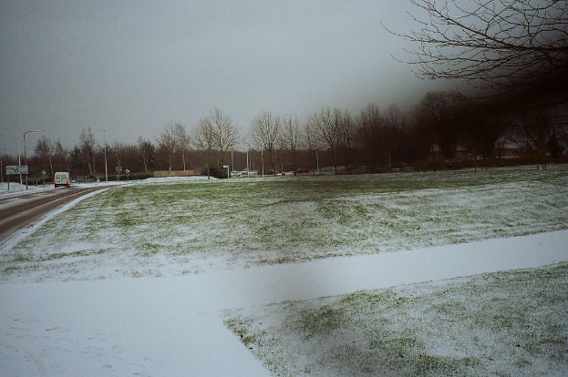 Eine schneebedeckte und neblige Landschaft mit Fahrzeugen auf der Straße und Bäumen im Hintergrund.