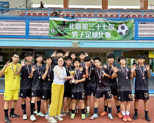 Eine Gruppe junger Männer in Fußballtrikots steht zusammen auf einem Feld, hält einen Pokal und trägt Medaillen, mit einem Gebäude im Hintergrund, das eine 'Yokohama U-16-Jungenfußballmannschaft' zeigt.