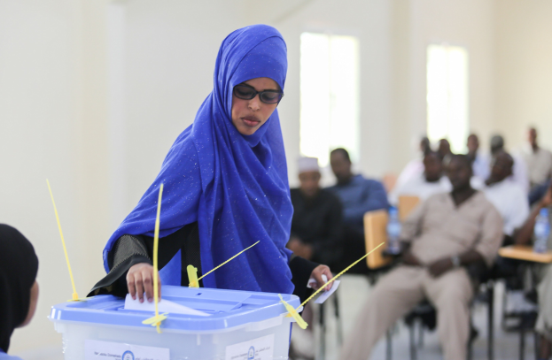 Eine Frau mit blauem Kopftuch gibt ihre Stimme an einer Wahllokal ab, während andere in der Nähe warten.
