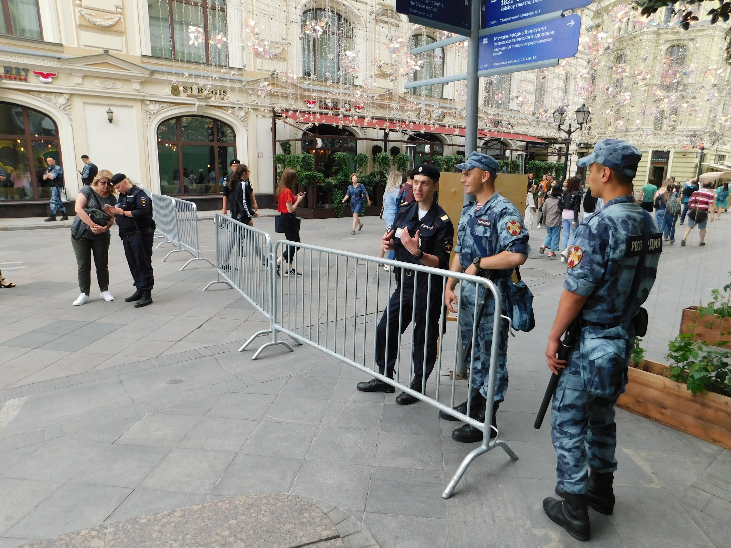 Polizeibeamte in Uniform hinter Absperrungen vor einer Menge stehend, einige mit Waffen, mit Gebäuden und Bäumen im Hintergrund während eines Einsatzes in Wien.