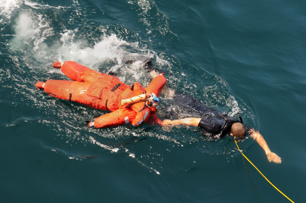 Retter in einer orangen Schwimmweste über einem Gewässer hängend.