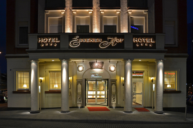 Das Essenerhof Hotel in Berlin, Deutschland, ein mehrstöckiges Gebäude mit Fenstern, Türen, Säulen, Laternen, einem Namensschild, einer Straße davor und Fahrzeugen auf der rechten Seite.