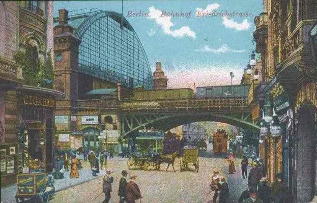 Schwarz-weiß-Postkarte einer belebten Berliner Straße mit Fußgängern, Pferdewagen, Gebäuden, Laternen, einer Brücke und bewölktem Himmel, mit Text oben.