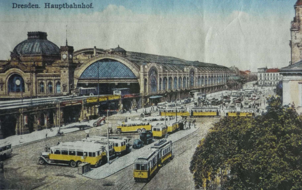 Schwarz-weiß-Postkarte vom Dresdner Hauptbahnhof: Eine belebte Straßen- und Fußgängerszene mit Fahrzeugen, Menschen, Bäumen, Gebäuden und einem bewölkten Himmel.