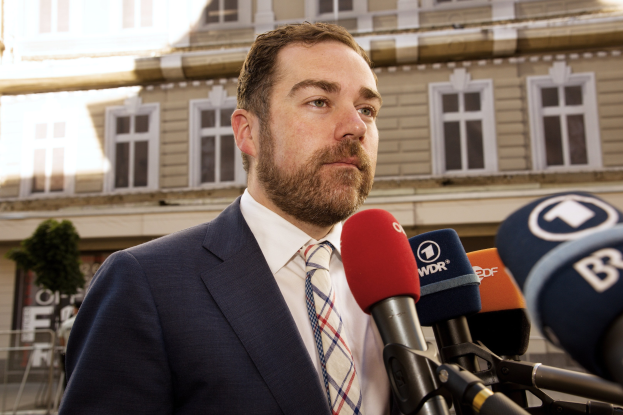 Ein Mann im Anzug spricht zu den Medien vor einem Gebäude, wahrscheinlich wegen einer dreijährigen Haftstrafe.