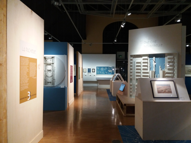 Ein Raum voller verschiedener Kunstwerke, darunter gerahmte Fotos, Texttafeln, Deckenbeleuchtung und ein Teppichboden, was auf eine Ausstellung im Museum of Modern Art hindeutet.