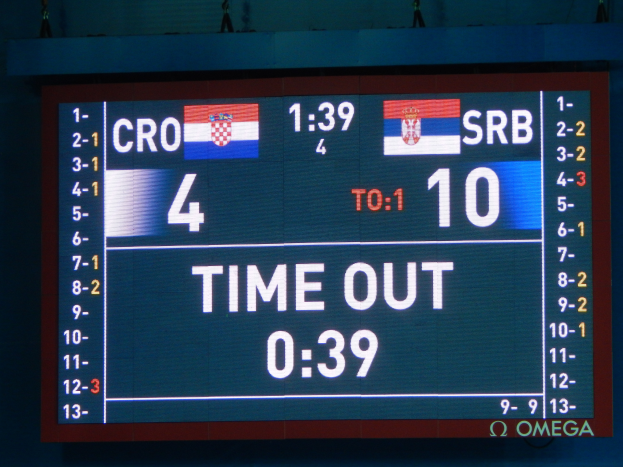 Ein großes elektronisches Scoreboard mit der Aufschrift "Kroatien vs. Serbien" mit Zahlen, Text und Flaggen, mit einigen Zuschauern oben im Bild.