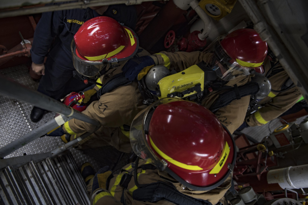 Feuerwehrleute in Schutzausrüstung bei der Arbeit an einem Löschfahrzeug mit Rohren und Equipment im Hintergrund.