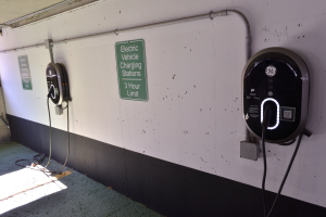 Ein Elektrofahrzeug-Ladestation in einer Tiefgarage mit zwei Ladegeräten an der Wand und Schildern mit Text darauf, der Boden ist unten im Bild zu sehen.