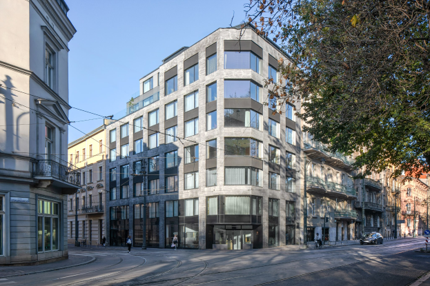 Großes modernes Bürogebäude mit zahlreichen Fenstern, umgeben von Straßeninfrastruktur einschließlich Masten, Lampen, Kabeln und Fahrzeugen, mit Fußgängern, Bäumen und einem bewölkten Himmel im Hintergrund.