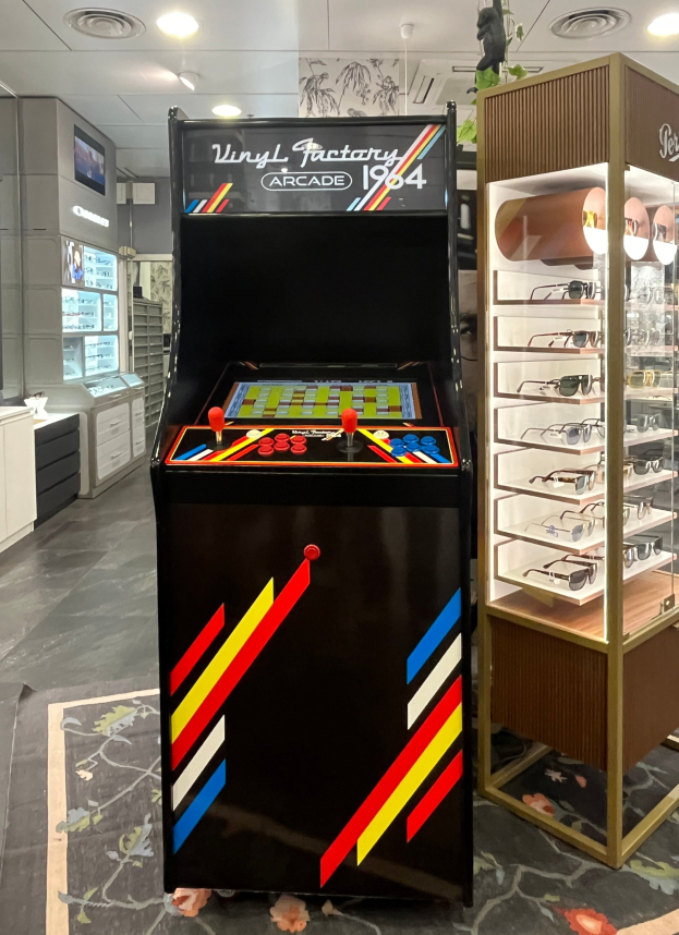 Ein Retro-Laden mit einem alten Arcade-Spielautomaten, einer Brillenauslage, Schränken, einem Fernseher und Deckenbeleuchtung im Hintergrund.