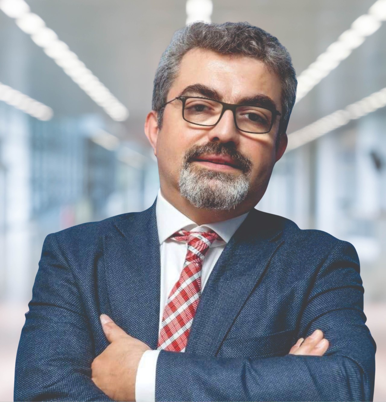 Ein Mann in Anzug und Krawatte mit verschränkten Armen, der eine Brille trägt und vor einem unscharfen Hintergrund steht, mit Text unten, der ihn als neu ernannten Marketingchef identifiziert.