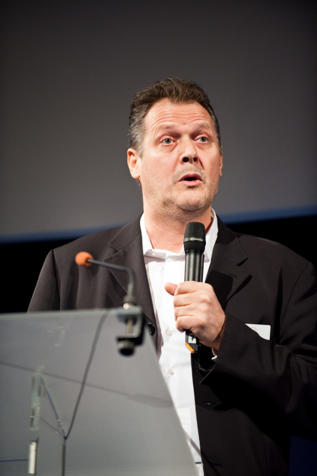 Ein Mann in einer schwarzen Jacke spricht in ein Mikrofon.