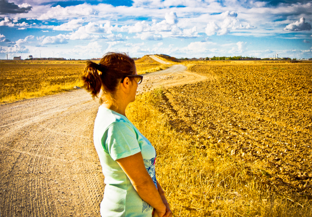 Eine Frau steht auf einem schlammigen Weg, umgeben von Landwirtschaftsland und Bäumen.