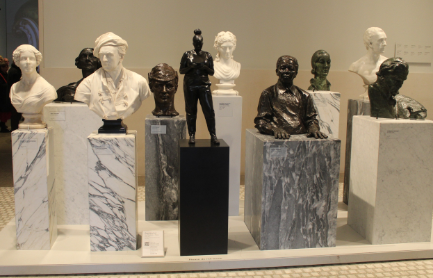 Gruppe detaillierter Büsten-Skulpturen in einem Museum ausgestellt, mit Besuchern im Hintergrund und einer Wand dahinter.