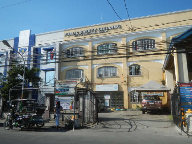 Gebäude für öffentliche Sicherheit von Bäumen, Straßeninfrastruktur, Fahrzeugen, Fußgängern und einem klaren Himmel umgeben
