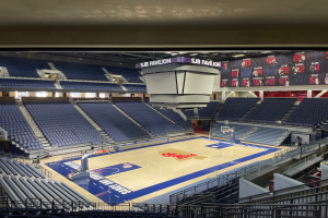 Eine große Halle mit einem Basketballfeld, Sitzplätzen und Anzeigetafeln, auf denen "SUB Pavilion an der University of Texas at Austin" steht.
