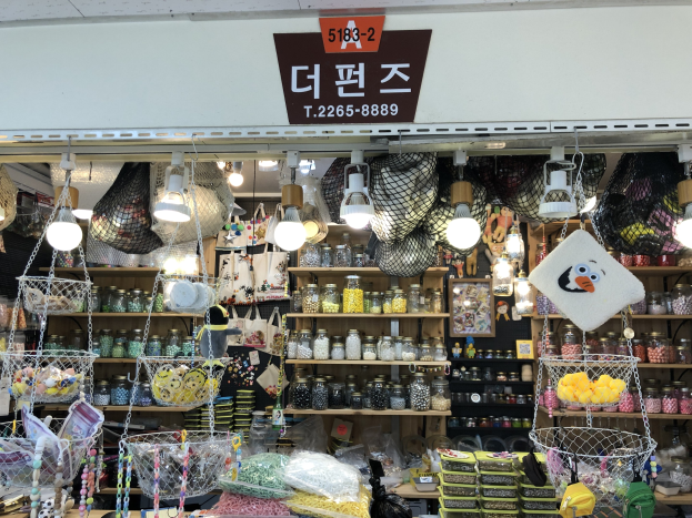 Ein unordentlicher Laden in Seoul, der verschiedene Gegenstände wie Körbe, Lichter, Flaschen und Spielzeuge auf Regalen ausstellt, mit einer Tafel öber dem Eingang, die ihn als einen der besten koreanischen Läden ausweist.