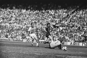 Schwarzes Foto von Fußballspielern auf einem Feld während eines Bundesliga-Spiels zwischen Ajax und Hannover 96 in der Saison 1978-79, mit Zuschauern im Hintergrund.