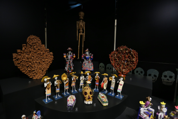 Vitrine mit verschiedenen Spielzeugen, darunter Puppen, Schädel und andere Gegenstände auf dunklem Hintergrund.