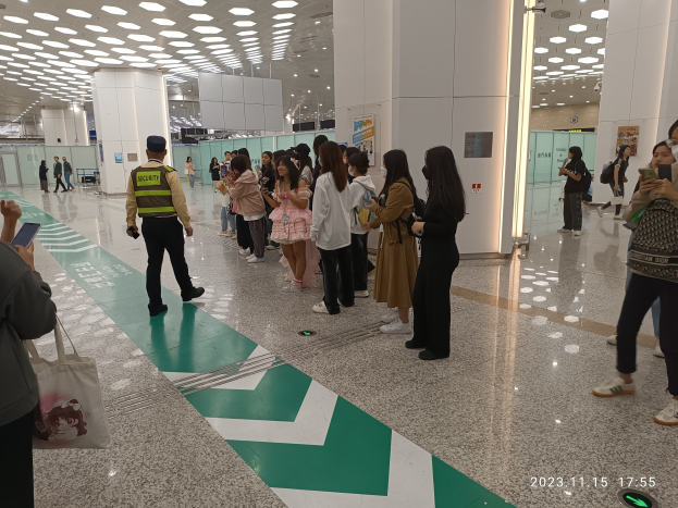 Menschen in der Schlange an einem Flughafen-Sicherheitscheck, mit Taschen und Mobiltelefonen, mit Säulen und Deckenlampen im Hintergrund.