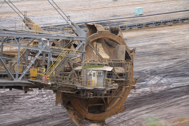 Großer Bagger auf einem Schmutzfeld mit Eisenstangen, Treppen, Geländern und anderen Gegenständen umgeben, umgeben von Blättern unten und Sand im Hintergrund, wahrscheinlich Teil eines Kohlebergwerks.